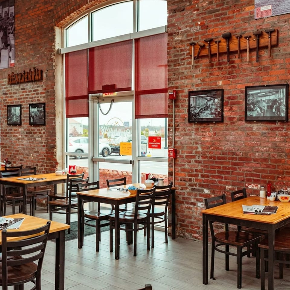 Restaurant interior with brick walls, wooden tables, chairs, and large windows with red blinds.