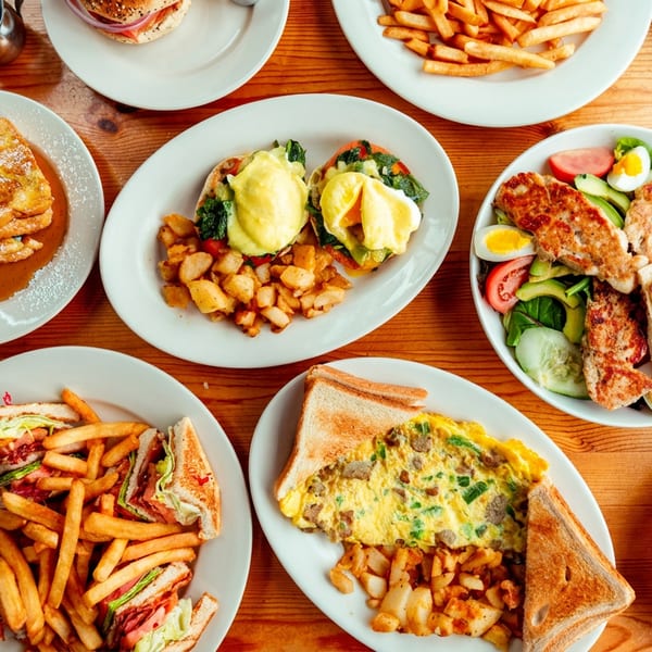 Overhead view of a wooden table laden with various breakfast and lunch dishes.