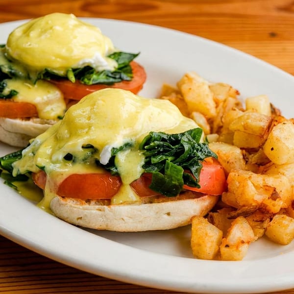 Eggs Benedict with spinach, tomatoes, and hollandaise sauce, served with crispy home fries.