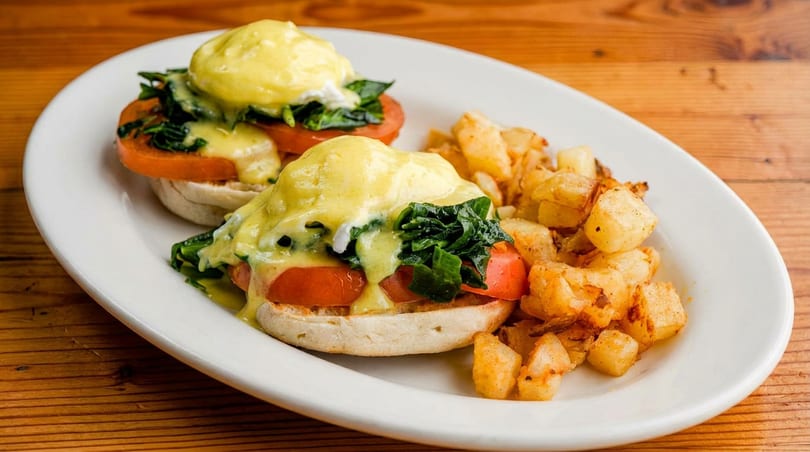 Eggs Benedict with spinach, tomatoes, and hollandaise sauce, served with crispy home fries.
