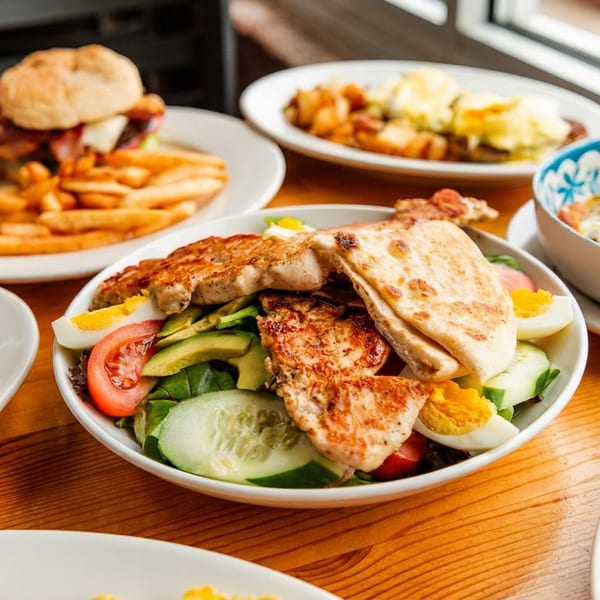 A wooden table laden with various brunch dishes, including a burger, salad, and eggs Benedict.