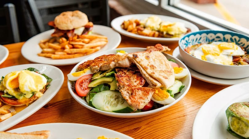 A table laden with various brunch dishes, including a burger, salad, and eggs Benedict.