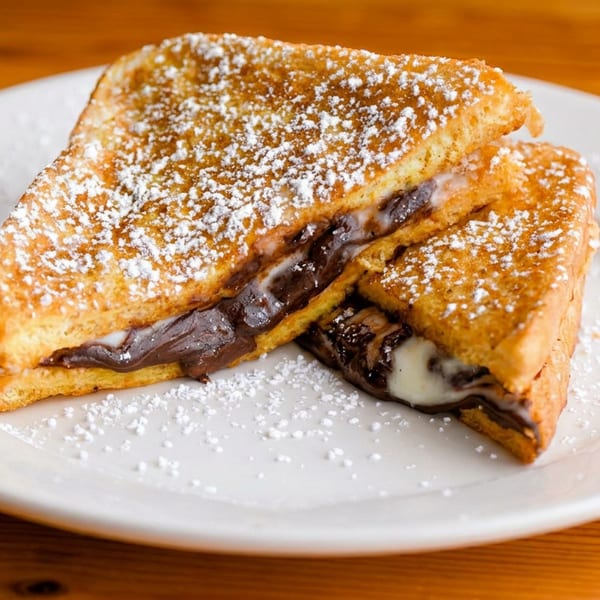 Two pieces of French toast, dusted with powdered sugar, filled with melted chocolate and marshmallow.